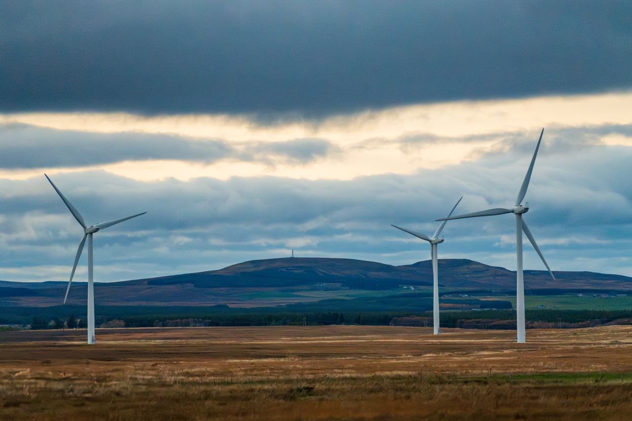 Wind turbines stand tall against a cloudy sky in an open landscape, symbolizing renewable energy.