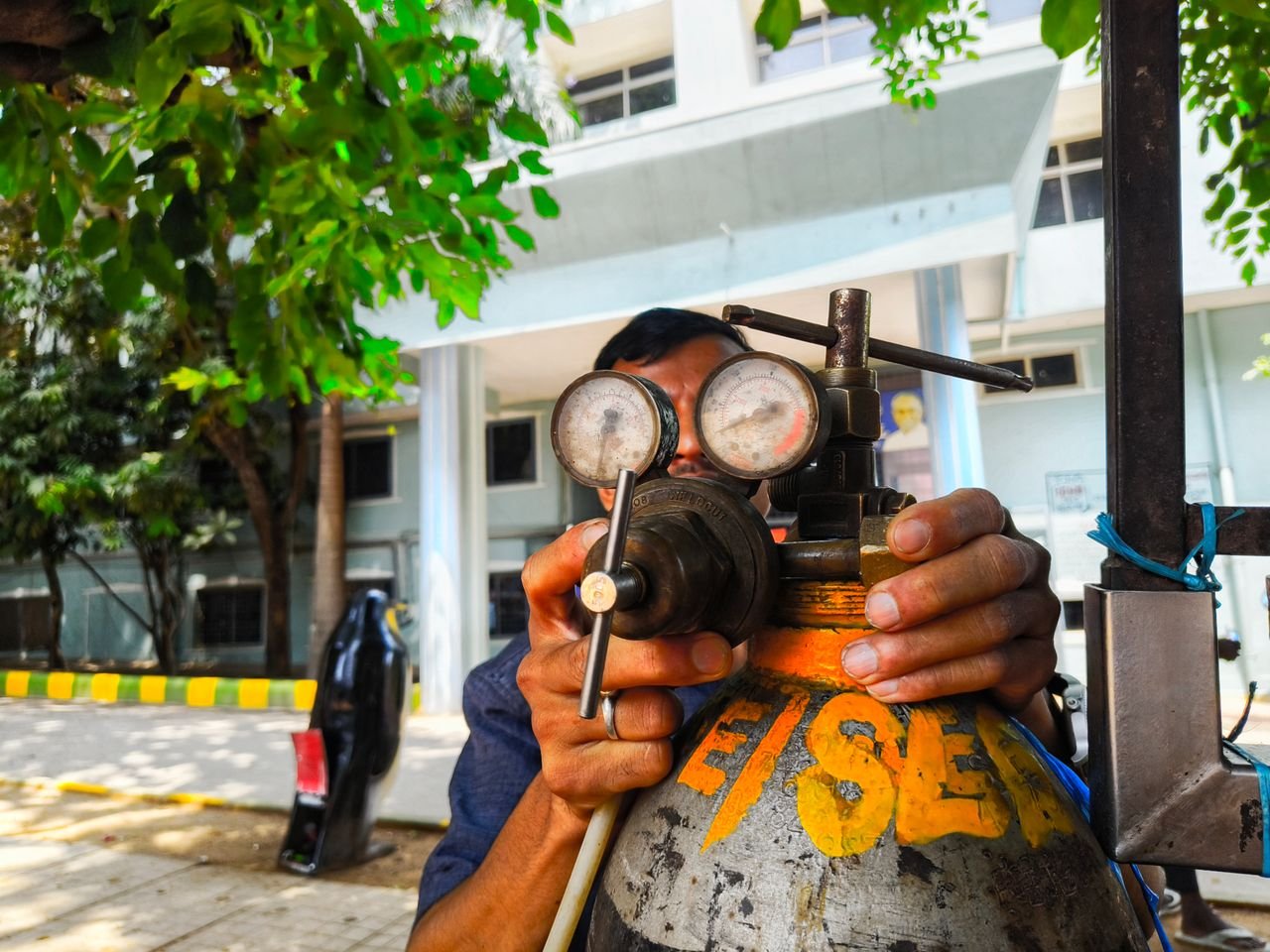 Close-up of a technician adjusting a gas regulator with pressure gauges in an outdoor setting in India.