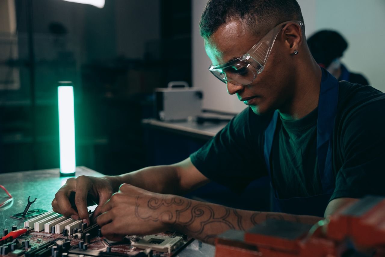 Technician in safety glasses concentrating on assembling a microchip in a contemporary workshop environment.